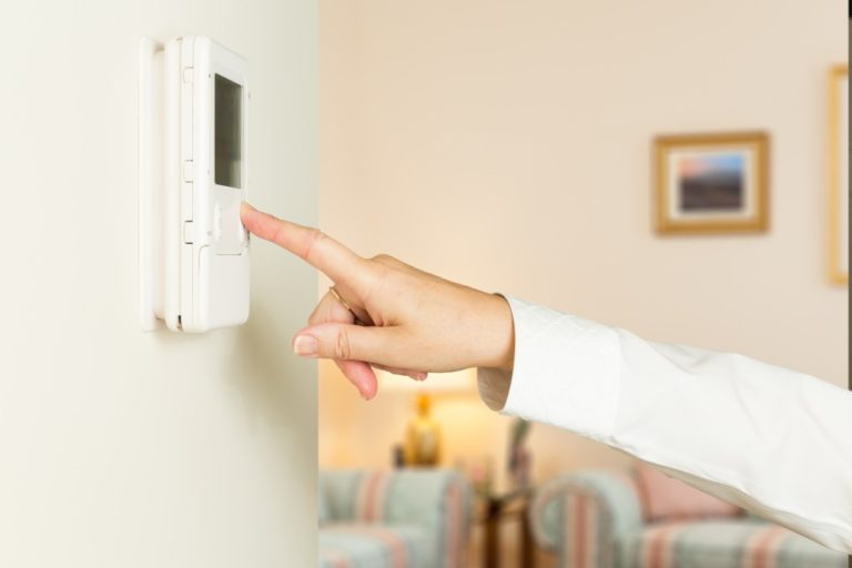 Woman adjusting thermostat of the room
